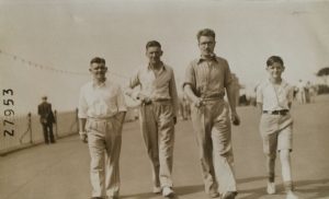 photo from the 1930s of three men and a boy in white shirts walking towards the camera in a line