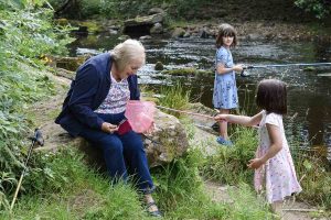 two children and grandmother at a river, child is showing grandmother her fishing net