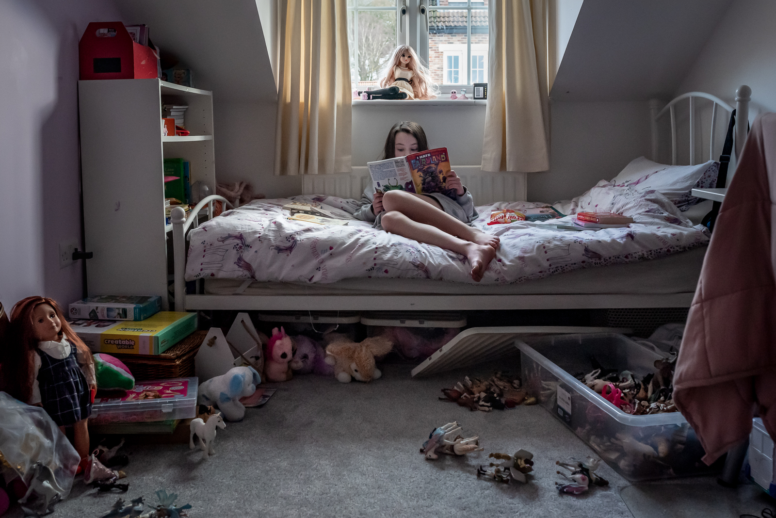 preteen environmental portrait in bedroom strewn with toys