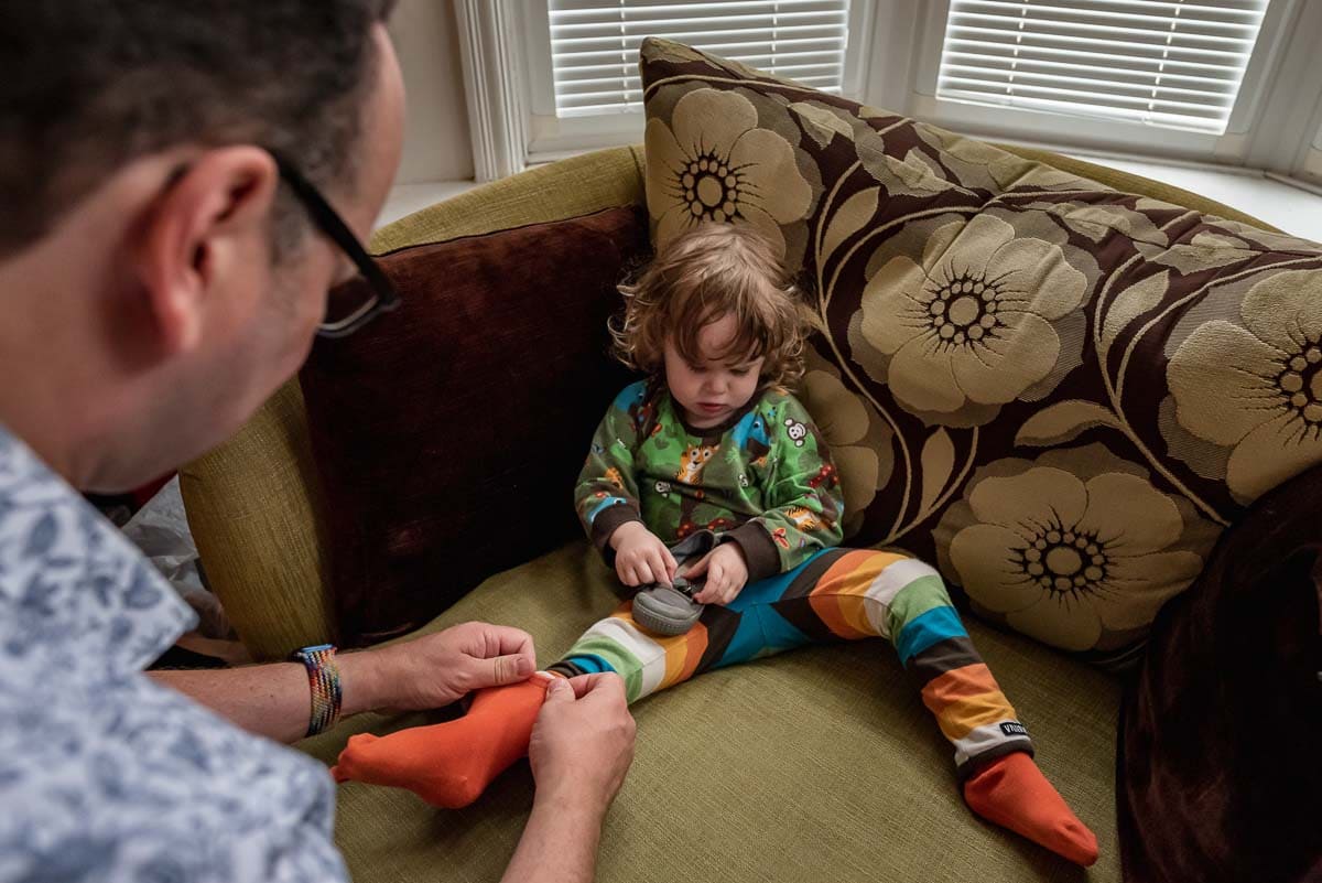 father puts socks on a grumpy toddler during a documentary family photography session