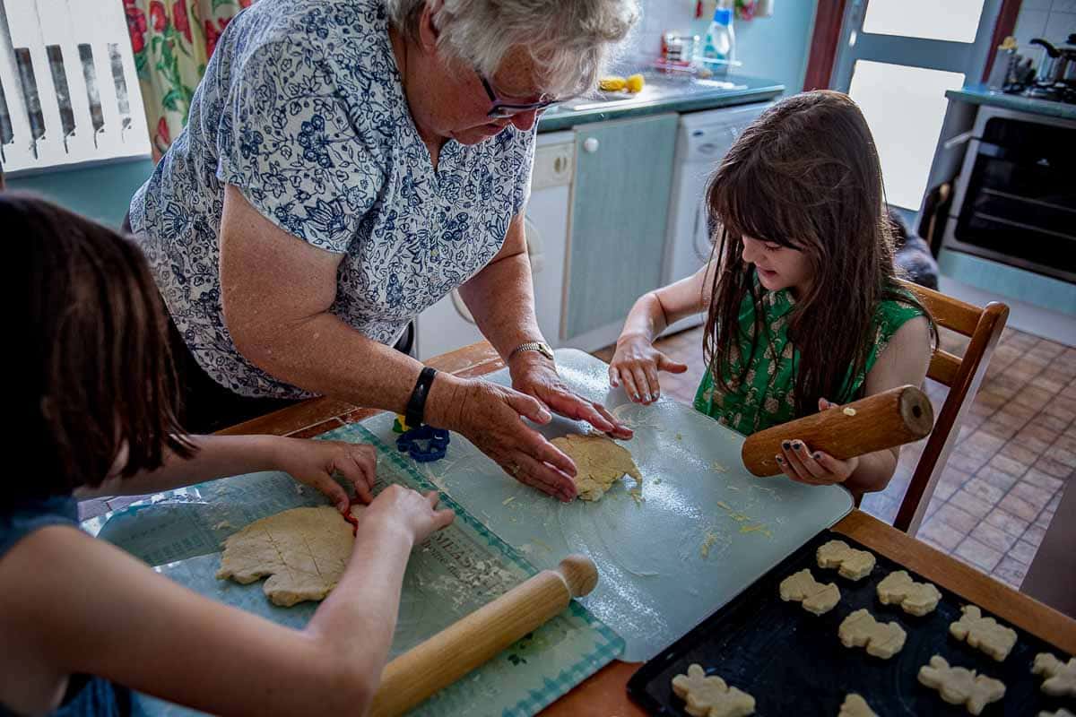 children baking with a grandmother rolling out biscuits at the kitchen table