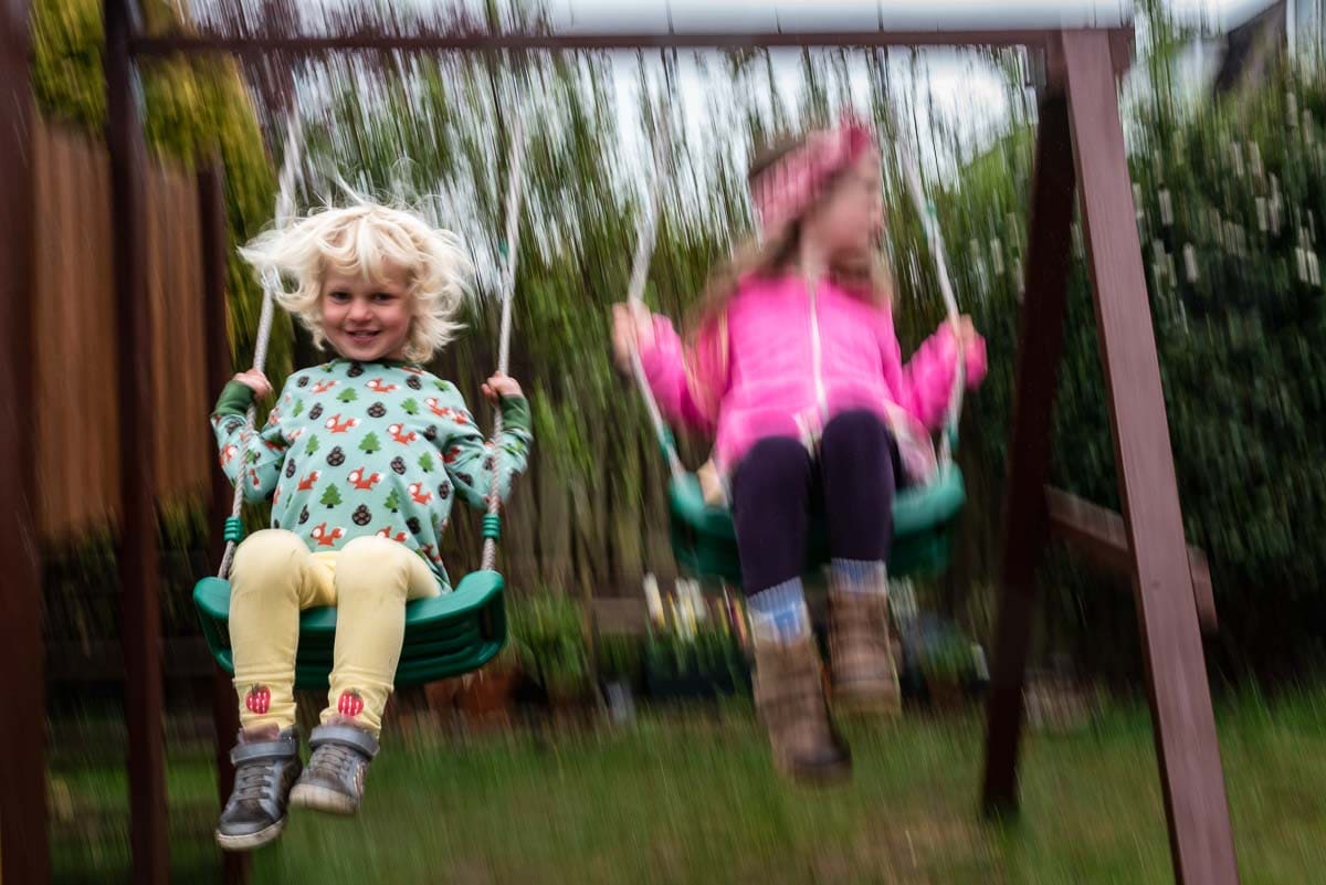 slow shutter image of siblings on swings in garden family photography session