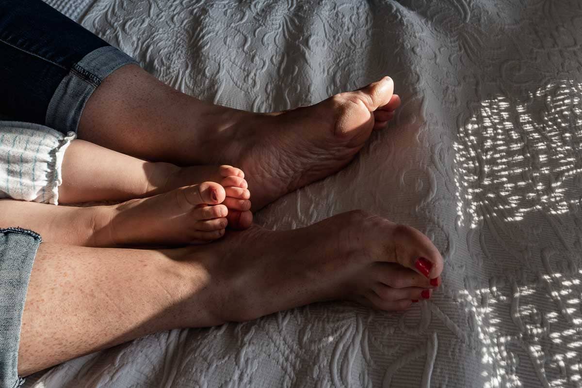 detail of mother and child's feet on bed in the evening sun