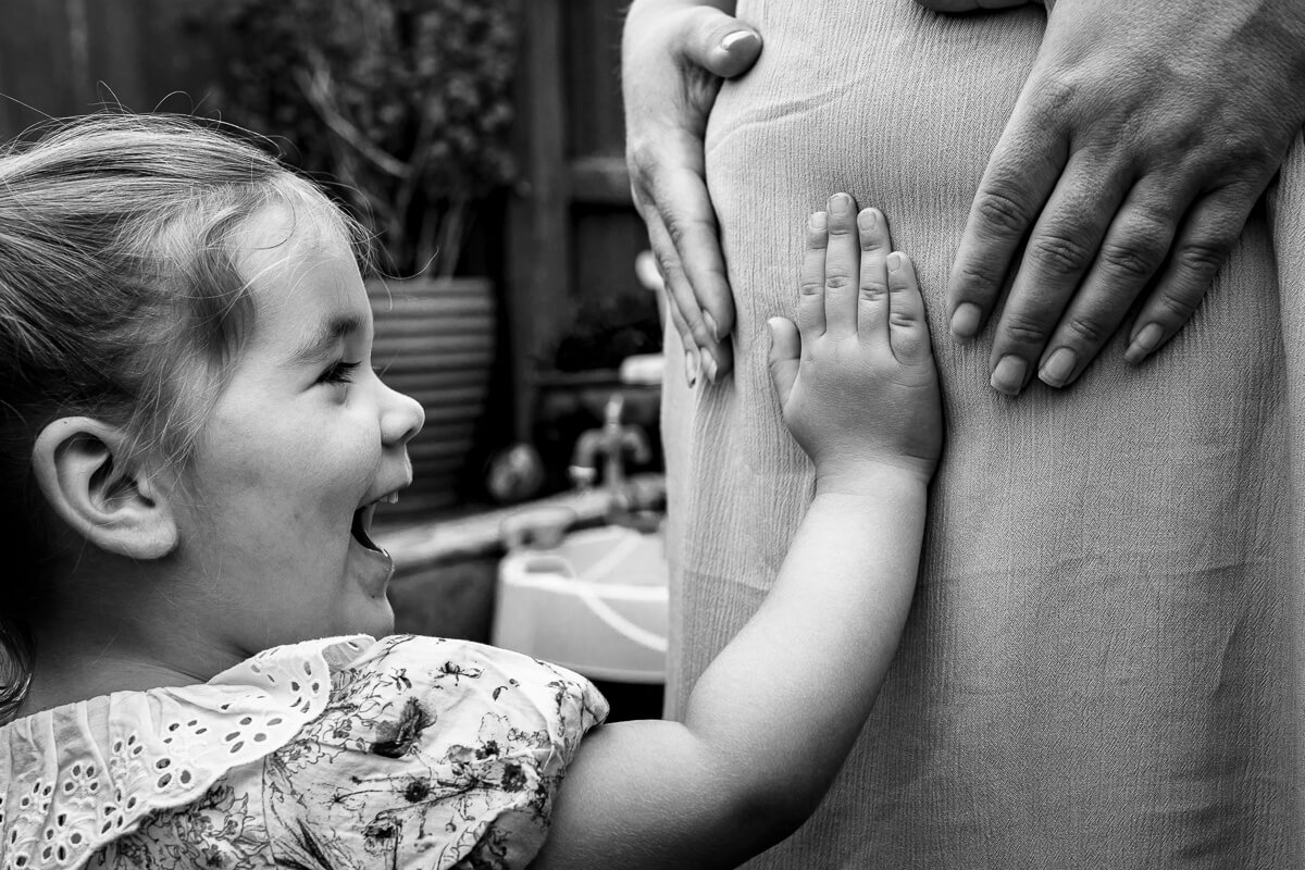 toddler touching mum's baby bump and laughing